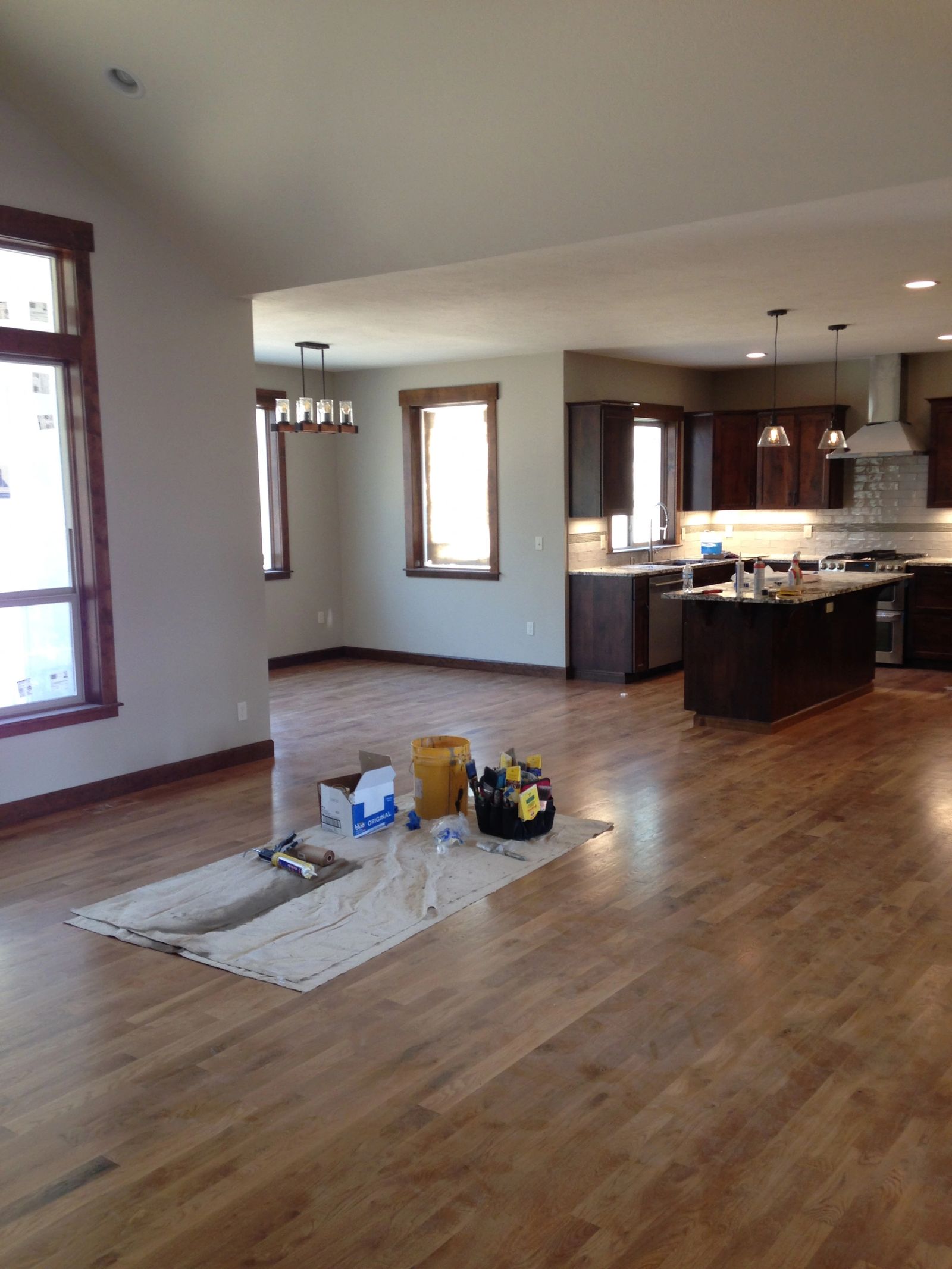 Open-concept interior with hardwood floors prepped and painted, drop cloths protecting the floor.