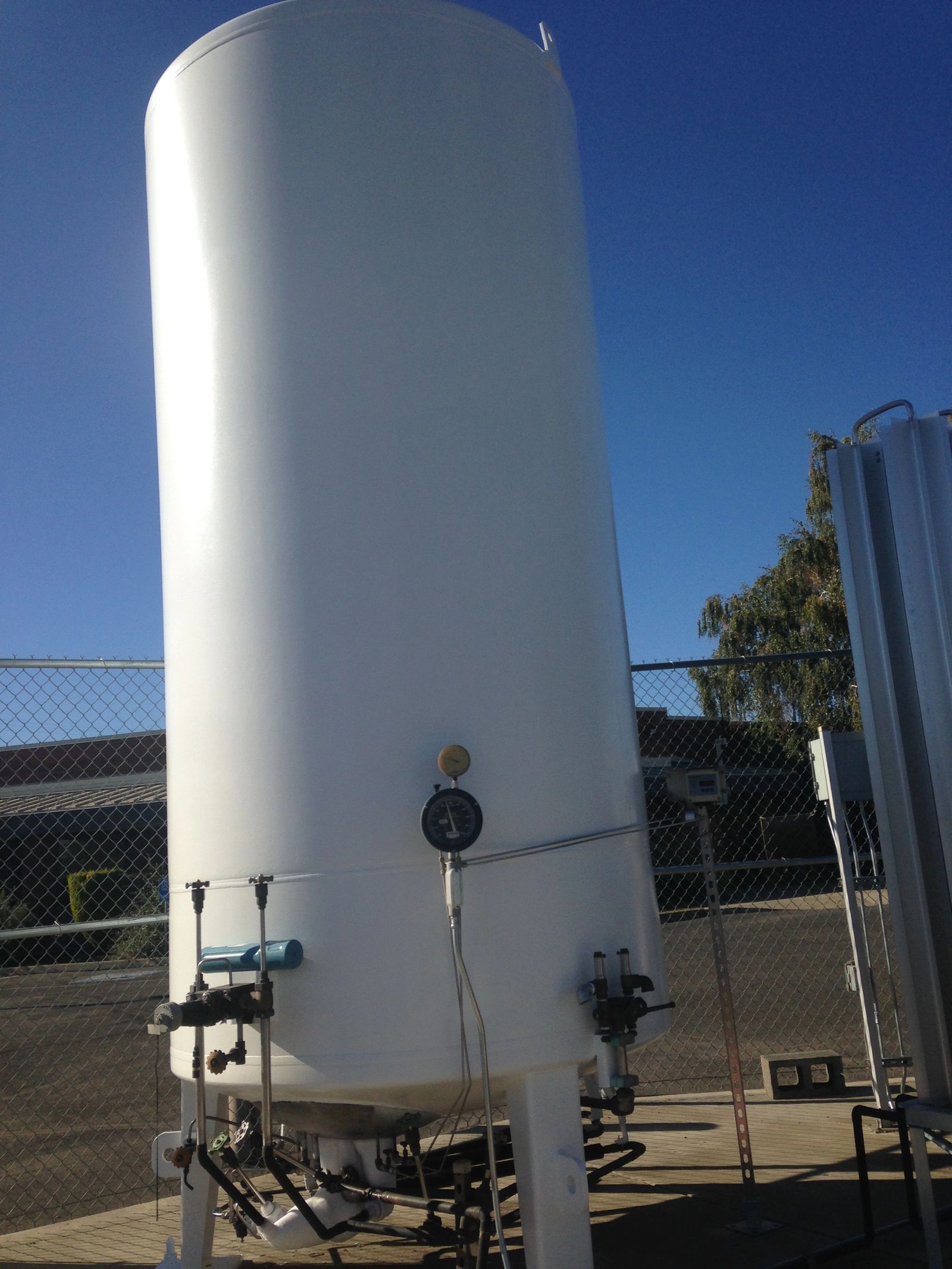 Industrial oxygen tank coated in white against a blue sky.
